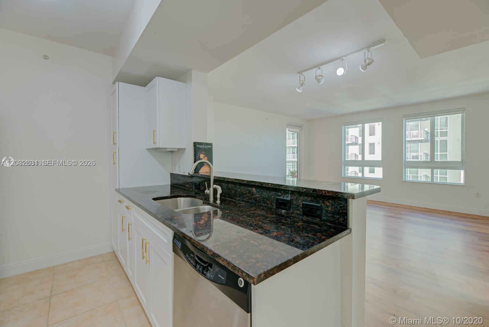 A kitchen with white cabinets, dark granite countertops, and stainless steel appliances overlooks a living area — 7350 SW 89th St # 2110S, Miami FL 33156, MIAMI, FL