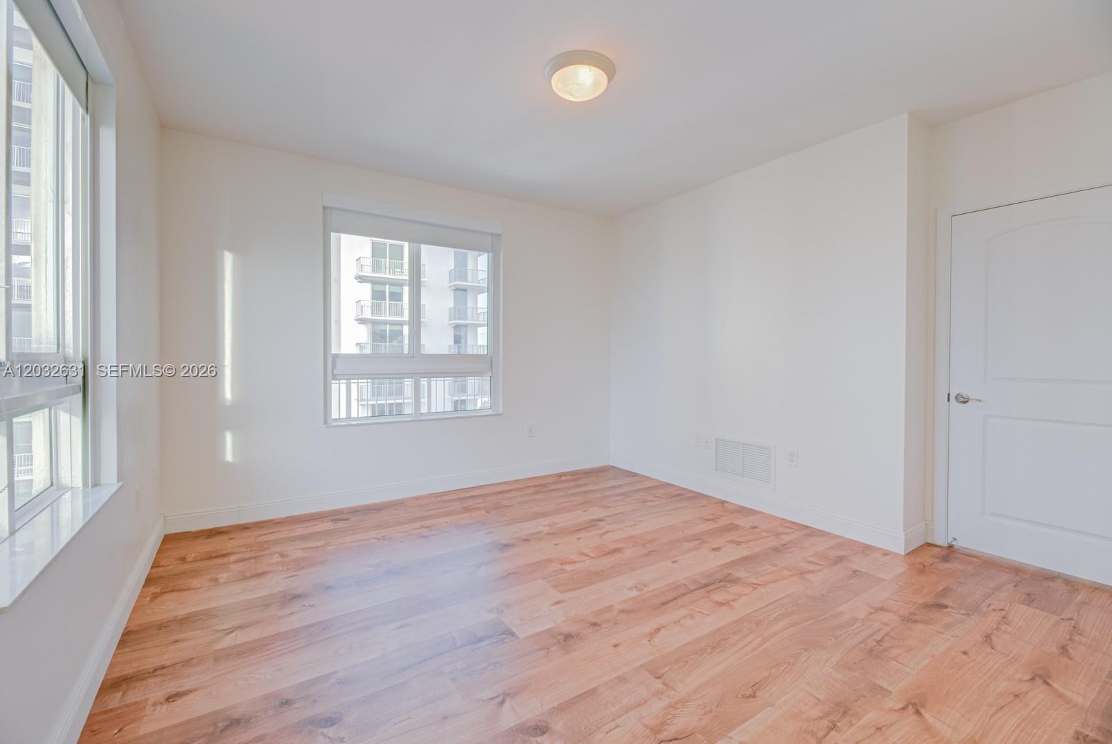 An empty room features light wood-look flooring, white walls, a ceiling light, and two windows — 7350 SW 89th St # 2110S, Miami FL 33156, MIAMI, FL