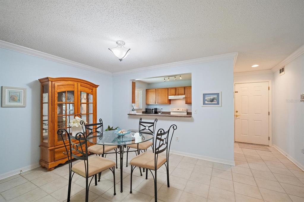 A dining area with a glass table, metal chairs, a wooden hutch, and a kitchen pass-through — 1927 TOUCAN WAY UNIT 306, SARASOTA, FL