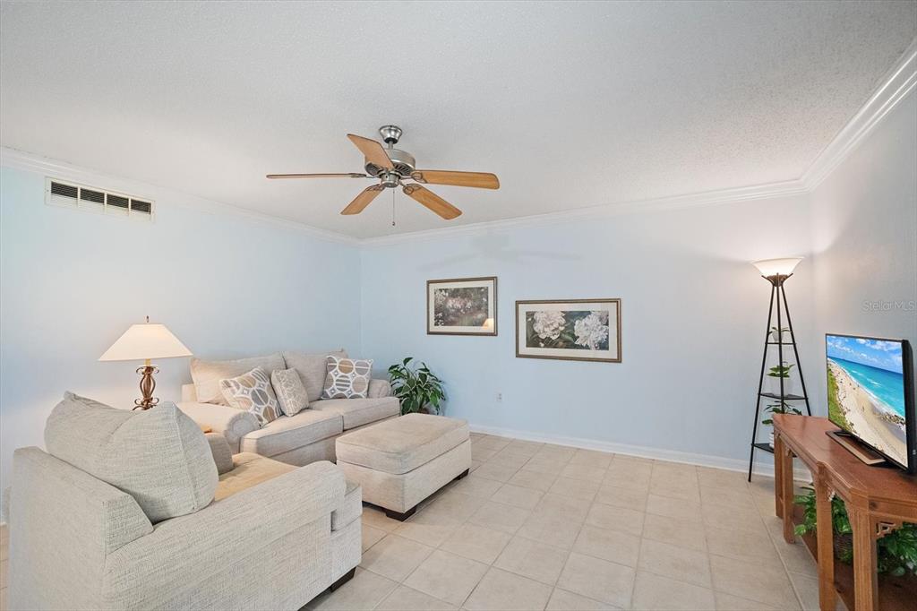 A living room features light blue walls, tile flooring, a ceiling fan, and neutral furniture — 1927 TOUCAN WAY UNIT 306, SARASOTA, FL