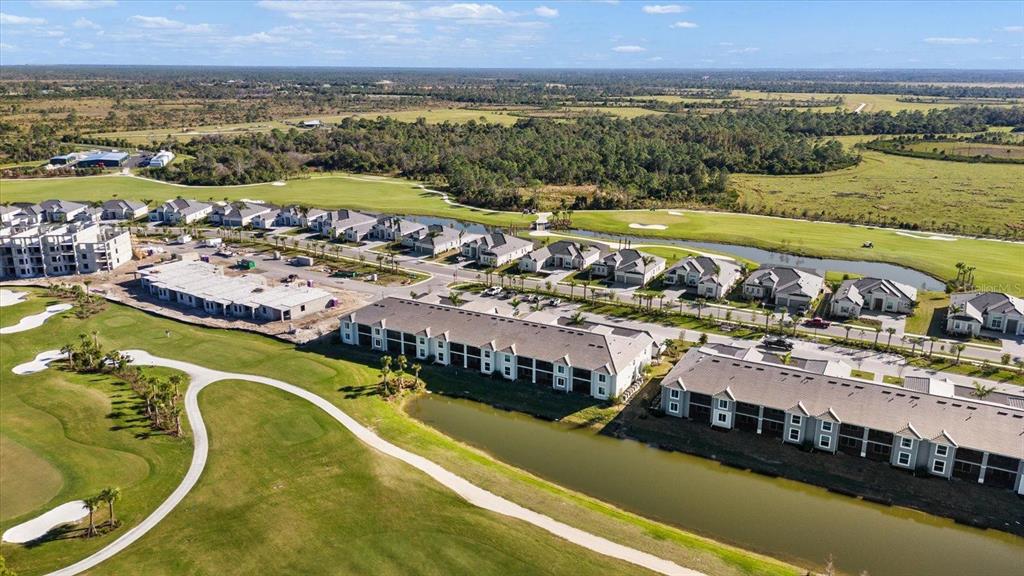 An aerial view shows residential townhomes and houses situated along a golf course and pond — 12390 WELLEN GOLF STREET UNIT 201, VENICE, FL