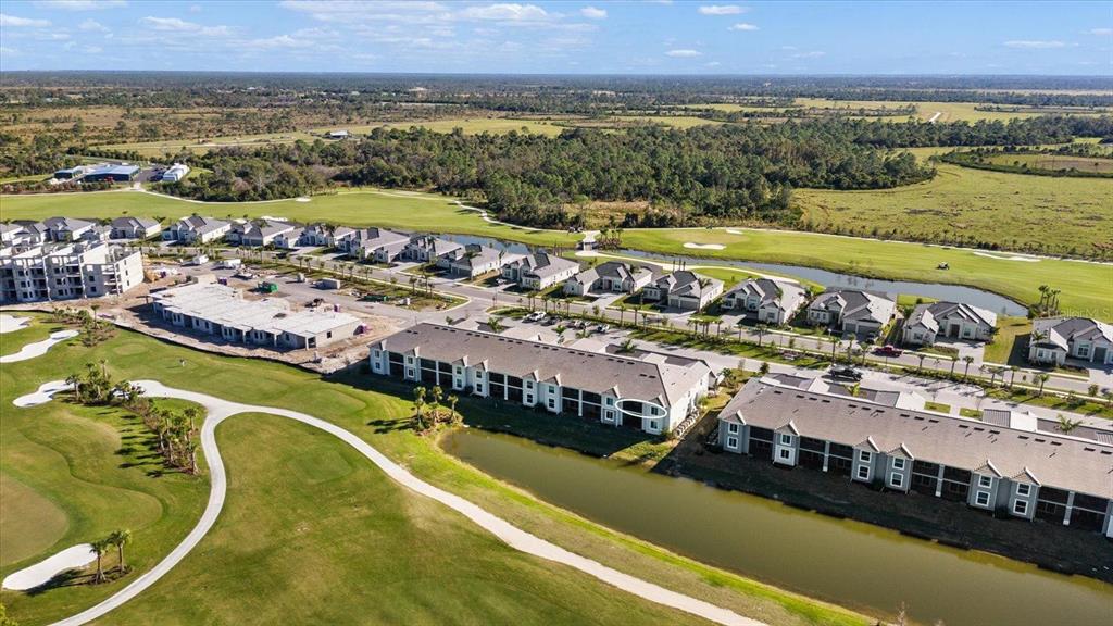 An aerial view shows multi-family residential buildings situated along a golf course and pond — 12390 WELLEN GOLF STREET UNIT 201, VENICE, FL