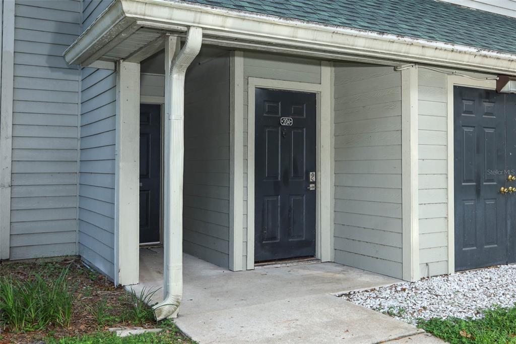 An exterior view of a building entrance featuring a dark door labeled 204 — 6070 WESTGATE DRIVE UNIT 204, ORLANDO, FL