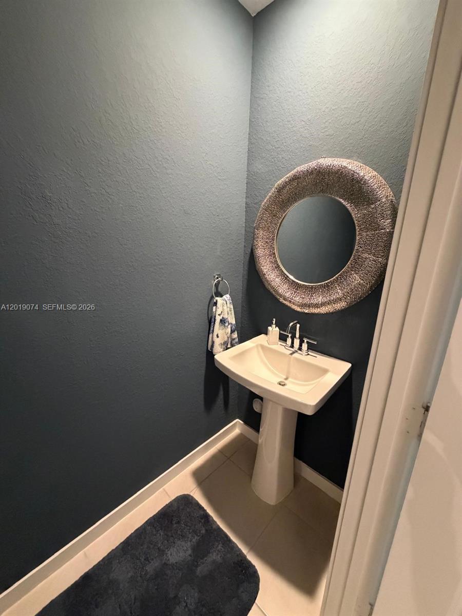 A small powder room features dark blue walls, a pedestal sink, and a round textured mirror — 1710 SE 9th Ave, Homestead FL 33034, HOMESTEAD, FL