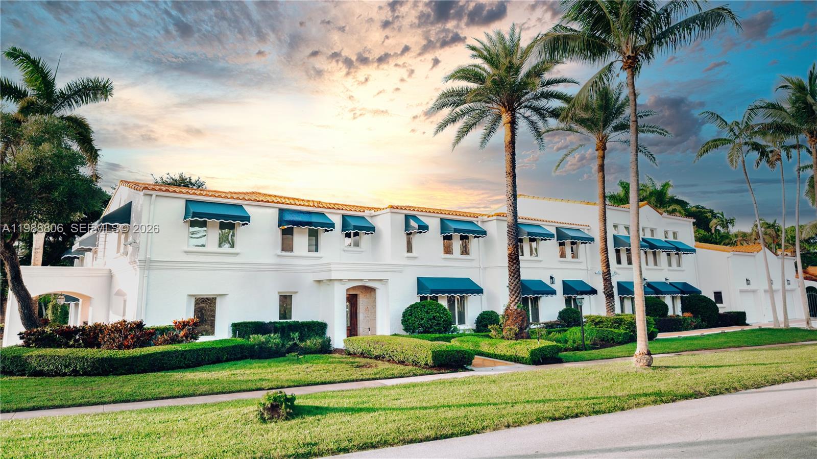 A two-story white house with blue awnings and palm trees under a sunset sky — 2525 Indian Mound Trl, Coral Gables FL 33134, CORAL GABLES, FL