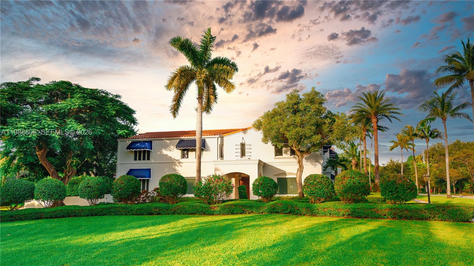 A two-story white house with blue awnings stands behind a manicured lawn and palm trees — 2525 Indian Mound Trl, Coral Gables FL 33134, CORAL GABLES, FL