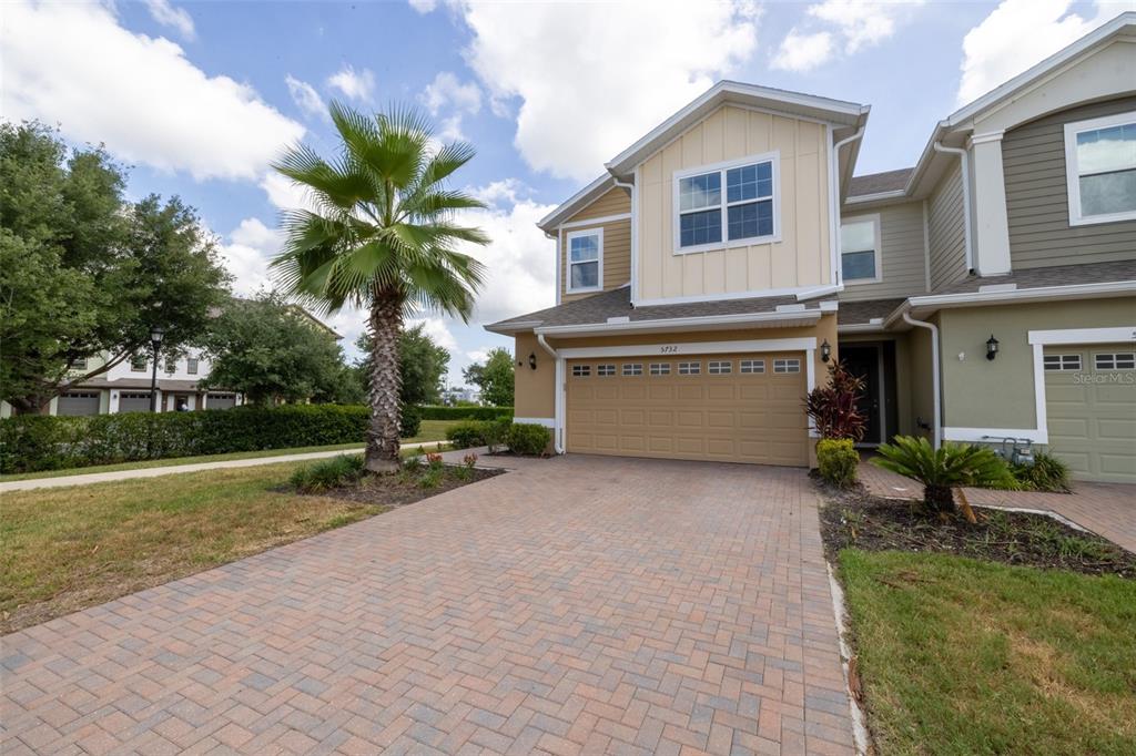 A two-story townhouse with a tan facade, a brick paver driveway, and a palm tree — 5732 SPOTTED HARRIER WAY, LITHIA, FL