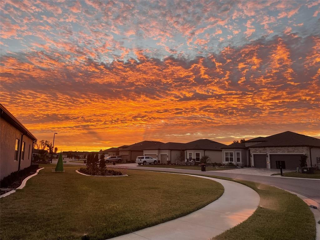 A suburban street scene features houses under a vibrant orange and pink sunset sky — 5475 SW 87TH TERRACE, OCALA, FL