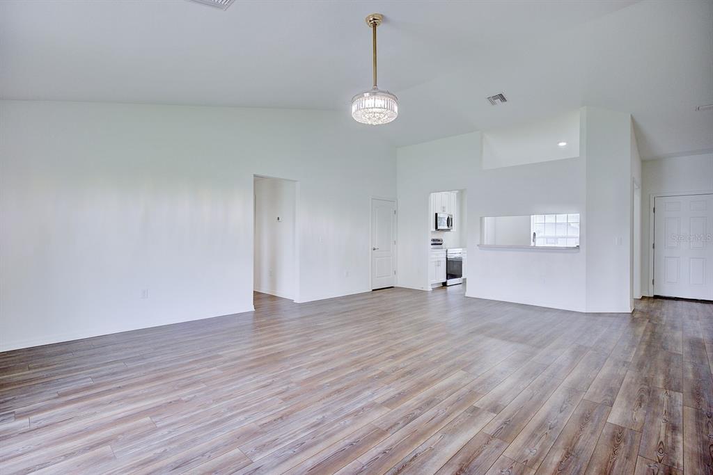 A spacious living area features vaulted ceilings, wood-look flooring, and a central crystal pendant light — 4550 SAN IGNACIO DRIVE, SEBRING, FL