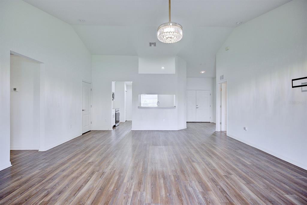 A spacious living area features high vaulted ceilings, light wood-look flooring, and a central chandelier — 4550 SAN IGNACIO DRIVE, SEBRING, FL