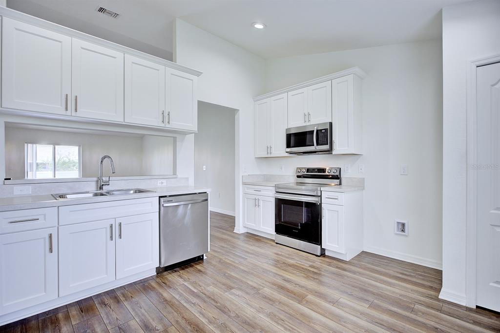 A kitchen with white cabinets, stainless steel appliances, and wood-look flooring — 4550 SAN IGNACIO DRIVE, SEBRING, FL