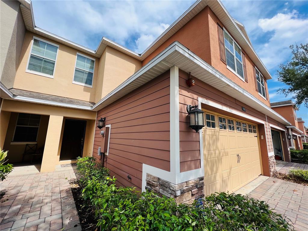 A two-story house exterior features a tan stucco facade, brown horizontal siding, and a garage — 1241 PRIORY CIRCLE, WINTER GARDEN, FL