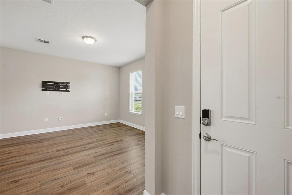 A room with wood-look flooring, a wall-mounted television bracket, and a white interior door — 14268 BRAEMAR STREET, WINTER GARDEN, FL