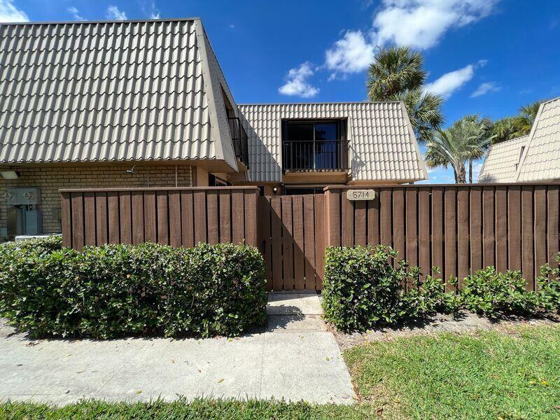 A brown wooden fence encloses the front patio of a two-story townhouse with a balcony — 5714 57th Way, West Palm Beach FL 33409, WEST PALM BEACH, FL