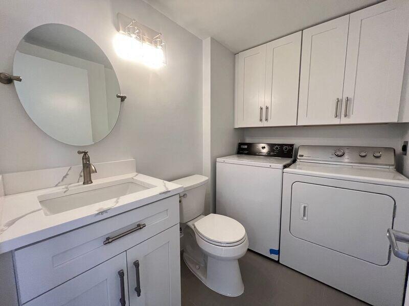 A bathroom with a vanity, toilet, and laundry appliances under white cabinets — 5714 57th Way, West Palm Beach FL 33409, WEST PALM BEACH, FL