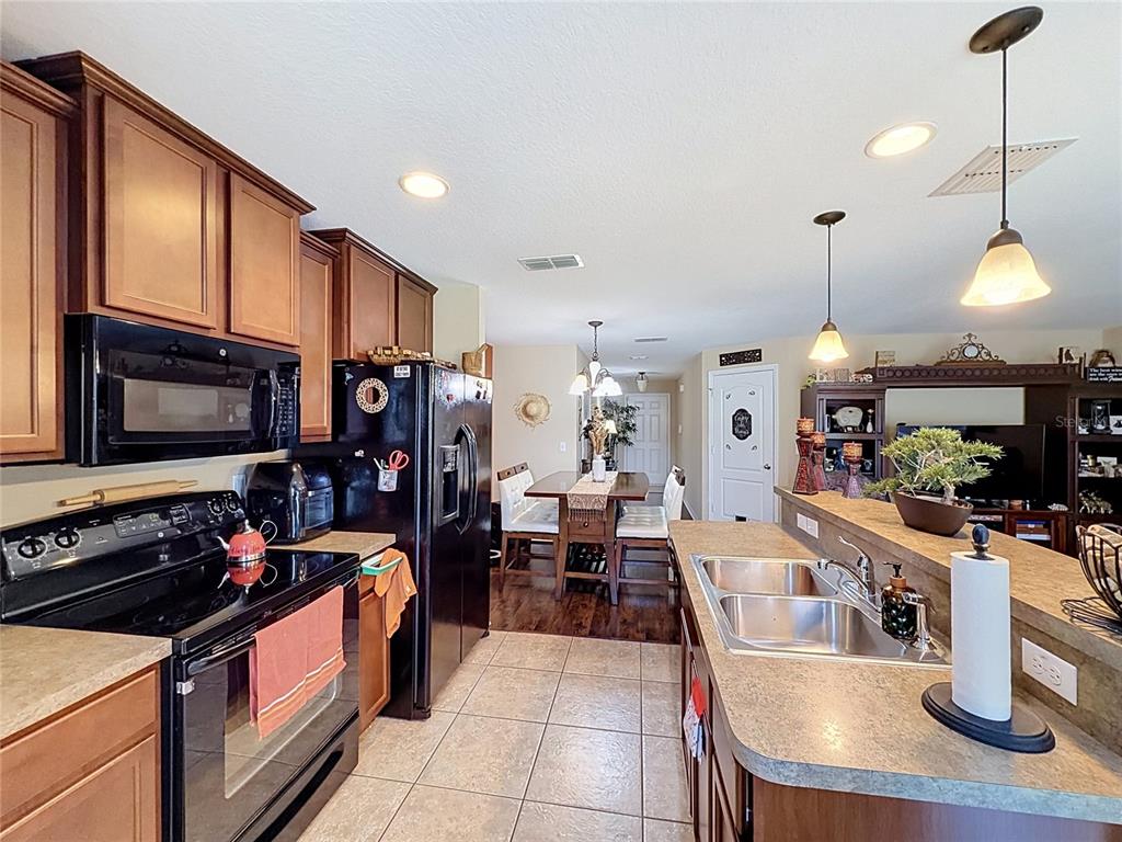 A kitchen with dark wood cabinets, black appliances, and a breakfast bar overlooks a dining area — 6420 WINDSOR LAKE CIRCLE, SANFORD, FL