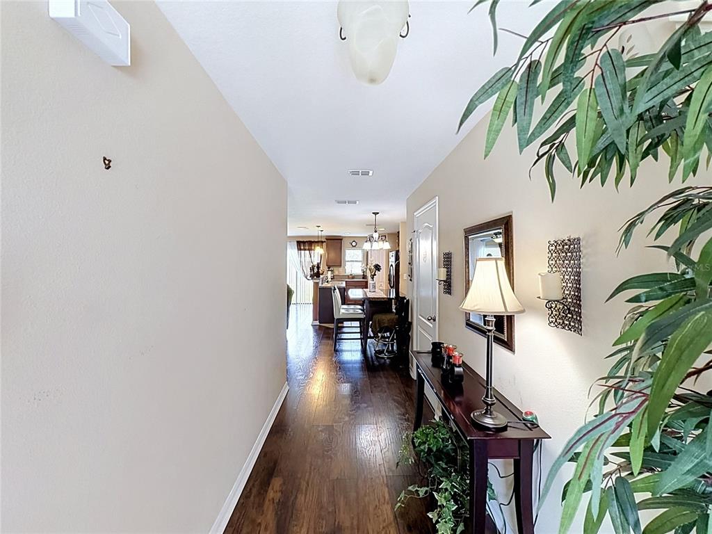 A hallway with dark wood flooring leads toward an open-concept kitchen and dining area — 6420 WINDSOR LAKE CIRCLE, SANFORD, FL