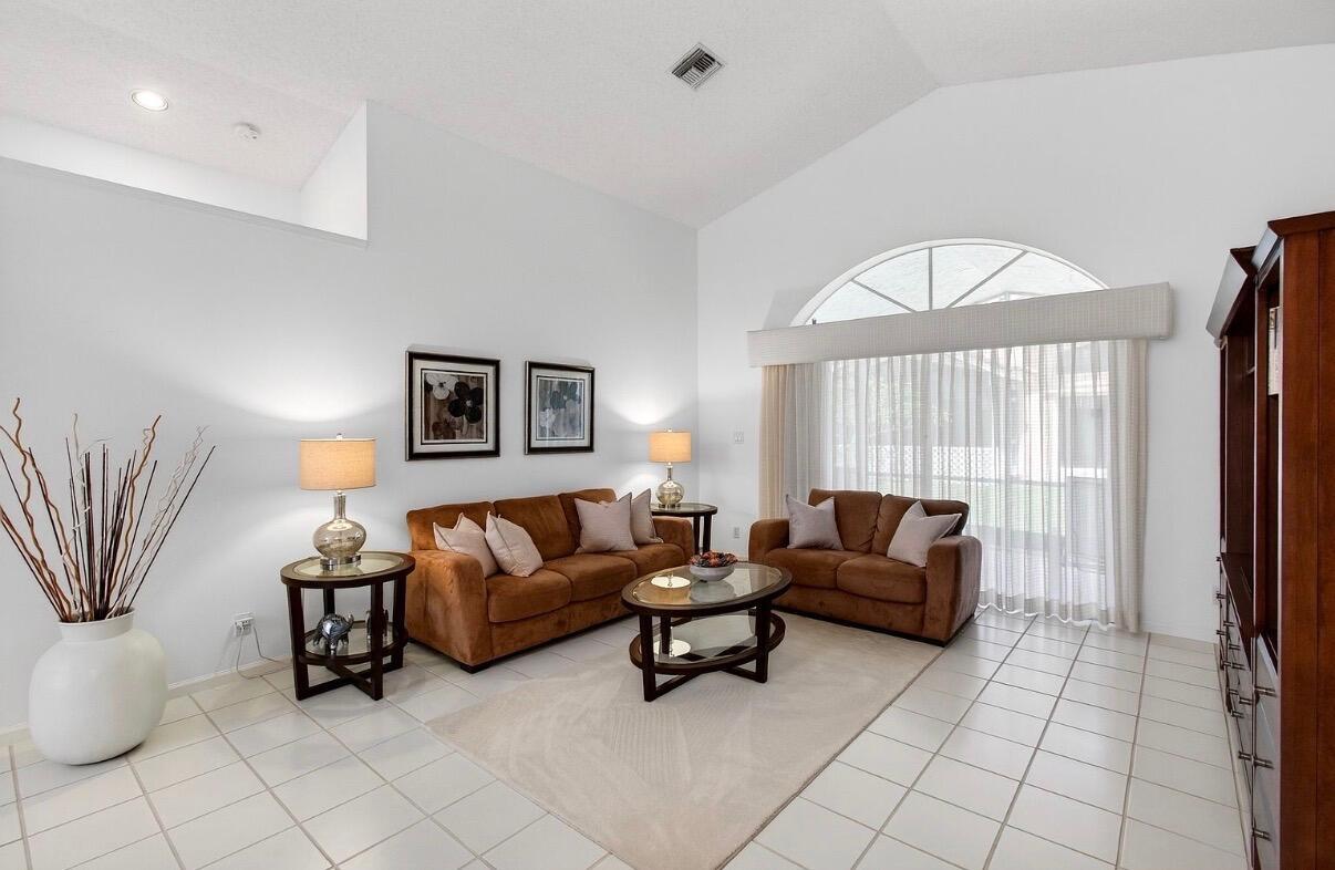 A living room with tile floors, brown sofas, and a large arched window with curtains — 14050 Fair Isle Drive, Delray Beach FL 33446, DELRAY BEACH, FL