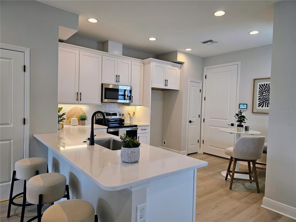 A modern kitchen features white cabinetry, quartz countertops, a breakfast bar, and light wood flooring — 7765 93RD STREET N, SEMINOLE, FL