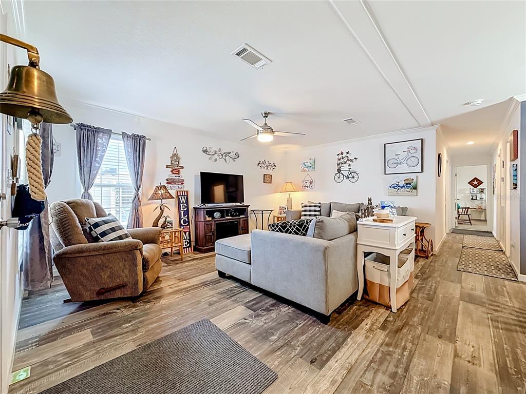 A living room features wood-look flooring, a gray sectional sofa, a recliner, and a television — 10485 HOLIDAY SHORES DRIVE UNIT 302, LARGO, FL