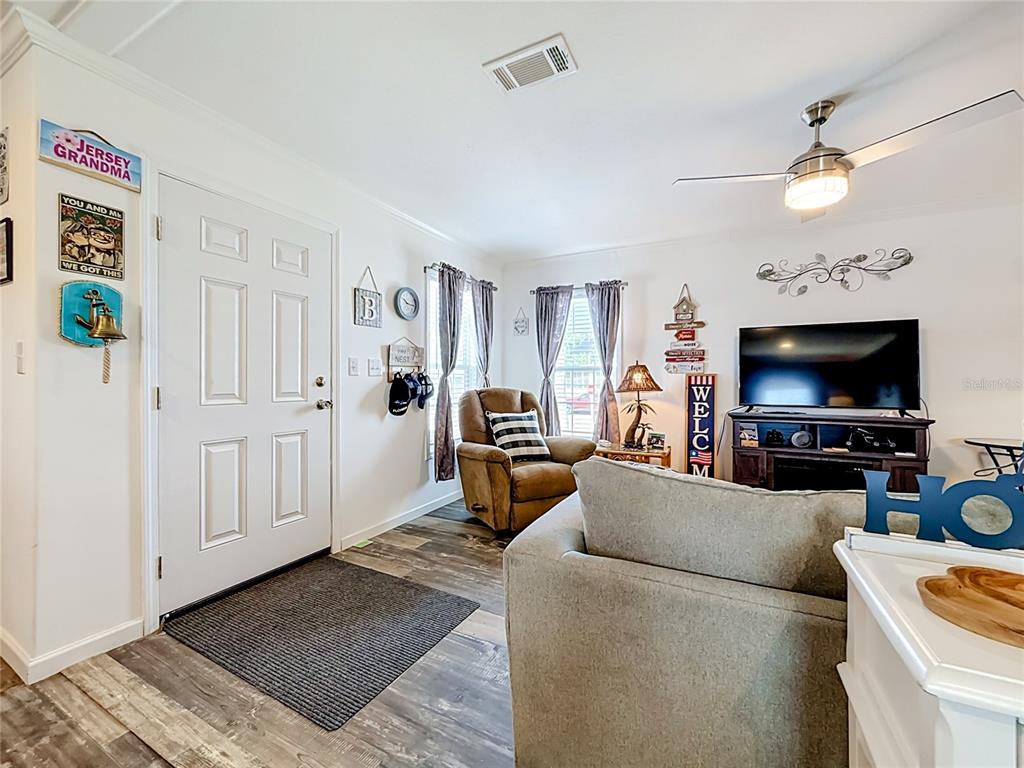 A living room features a front door, a brown recliner, a television, and wood-look flooring — 10485 HOLIDAY SHORES DRIVE UNIT 302, LARGO, FL