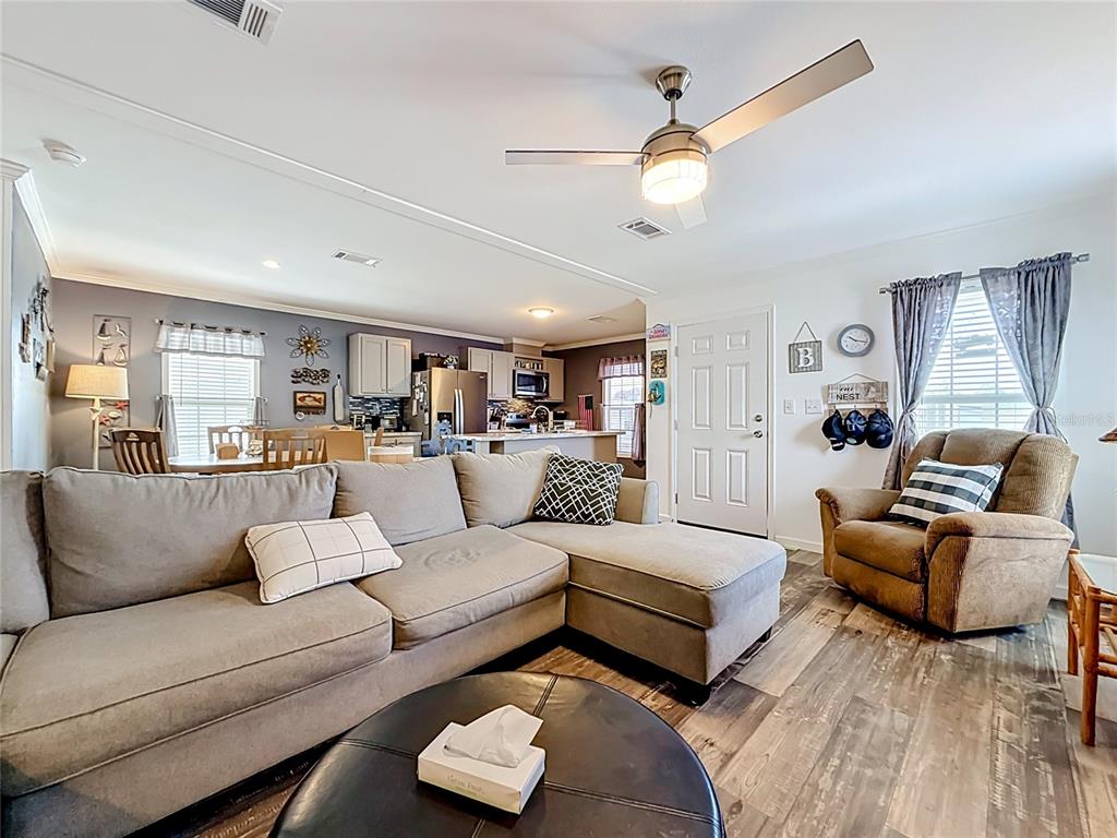 A living room with a sectional sofa, recliner, and ceiling fan opens into a kitchen — 10485 HOLIDAY SHORES DRIVE UNIT 302, LARGO, FL