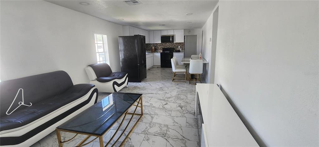An open-concept living and dining area features white marble-style tile flooring and black furniture — 3004 E DR MARTIN LUTHER KING JR BOULEVARD, TAMPA, FL