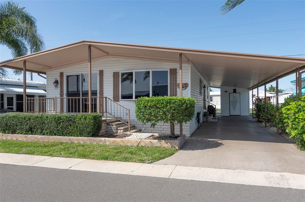 A single-story mobile home features a carport, a front porch, and a landscaped yard — 34236 CANAL DRIVE N UNIT 236, PINELLAS PARK, FL