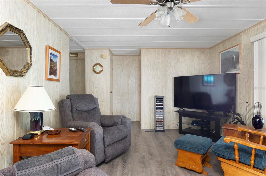 A living room features wood-paneled walls, a gray recliner, a television, and a ceiling fan — 34236 CANAL DRIVE N UNIT 236, PINELLAS PARK, FL
