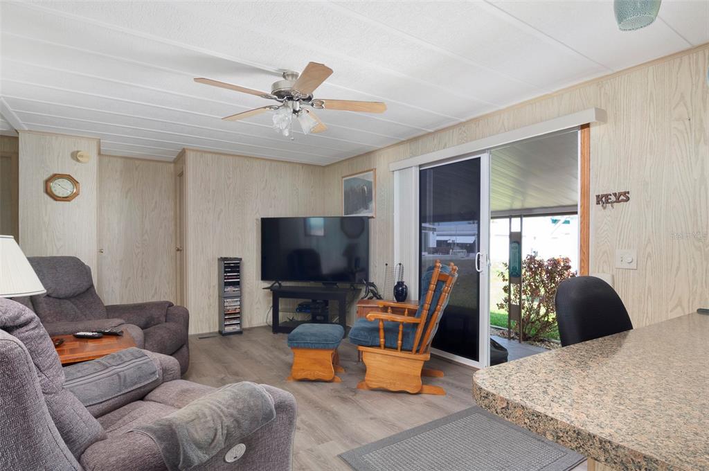 A living room features wood-paneled walls, a ceiling fan, a television, and a sliding glass door — 34236 CANAL DRIVE N UNIT 236, PINELLAS PARK, FL