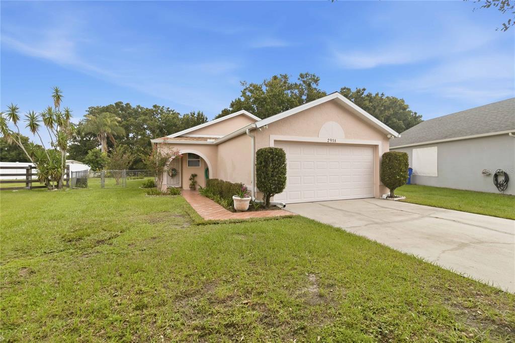 A single-story peach-colored house features a two-car garage, a brick walkway, and a grassy yard — 2918 CANOE CIRCLE, ST CLOUD, FL