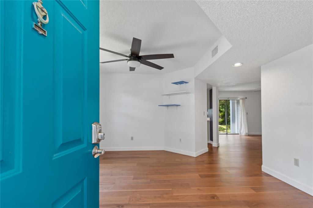An open teal door reveals a living area with wood floors, a ceiling fan, and shelves — 11800 PARK BLVD UNIT 401, SEMINOLE, FL
