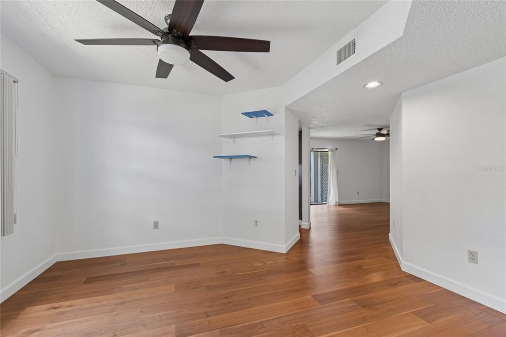 An empty room with hardwood floors, a ceiling fan, and floating shelves on the wall — 11800 PARK BLVD UNIT 401, SEMINOLE, FL