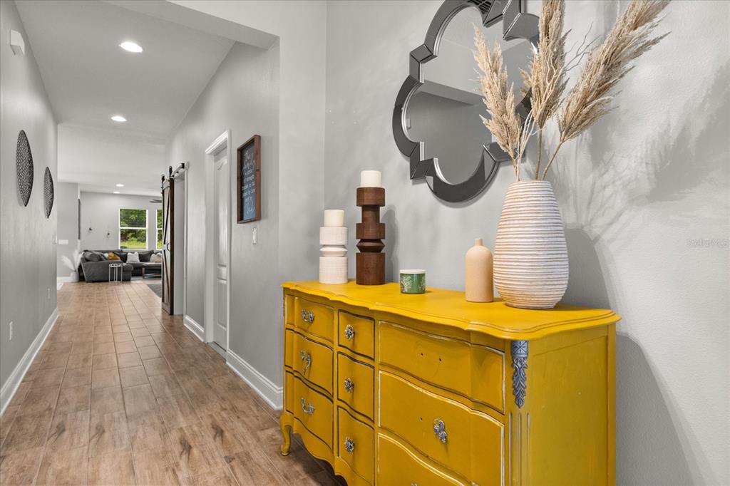 A hallway features wood-look tile flooring, a bright yellow dresser, and a decorative wall mirror — 31924 GEOFF WAY, SORRENTO, FL