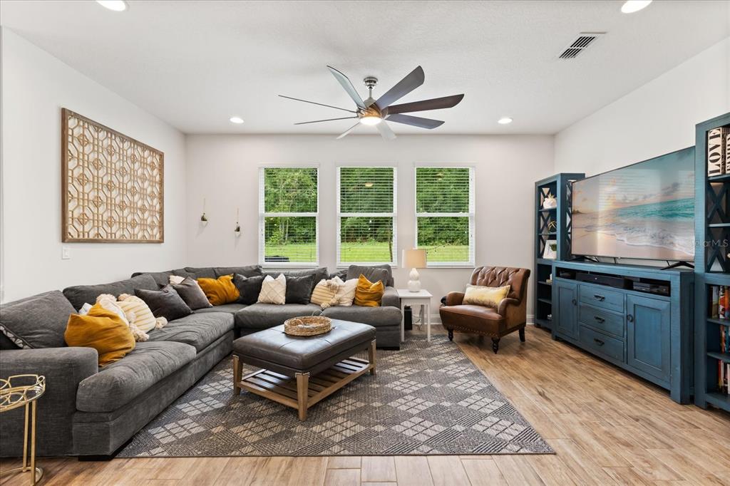 A living room features a large gray sectional, a blue media console, and wood flooring — 31924 GEOFF WAY, SORRENTO, FL