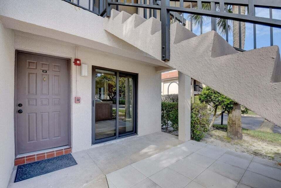 An exterior view of a ground-floor apartment entrance with a sliding glass door and stairs — 400 Club Circle # 101, Boca Raton FL 33487, BOCA RATON, FL