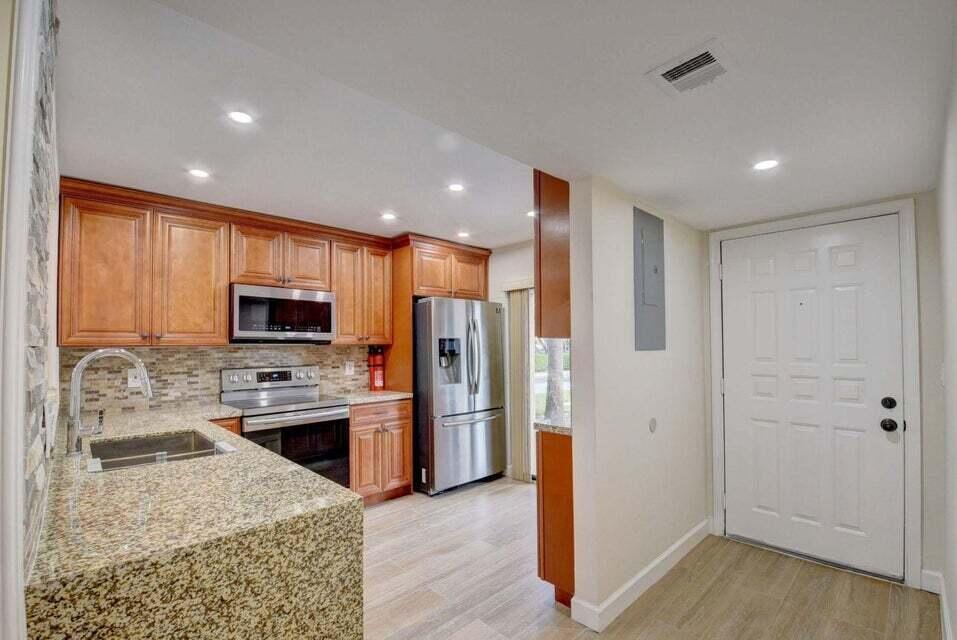 A kitchen with wood cabinets, granite countertops, stainless steel appliances, and an adjacent entry door — 400 Club Circle # 101, Boca Raton FL 33487, BOCA RATON, FL
