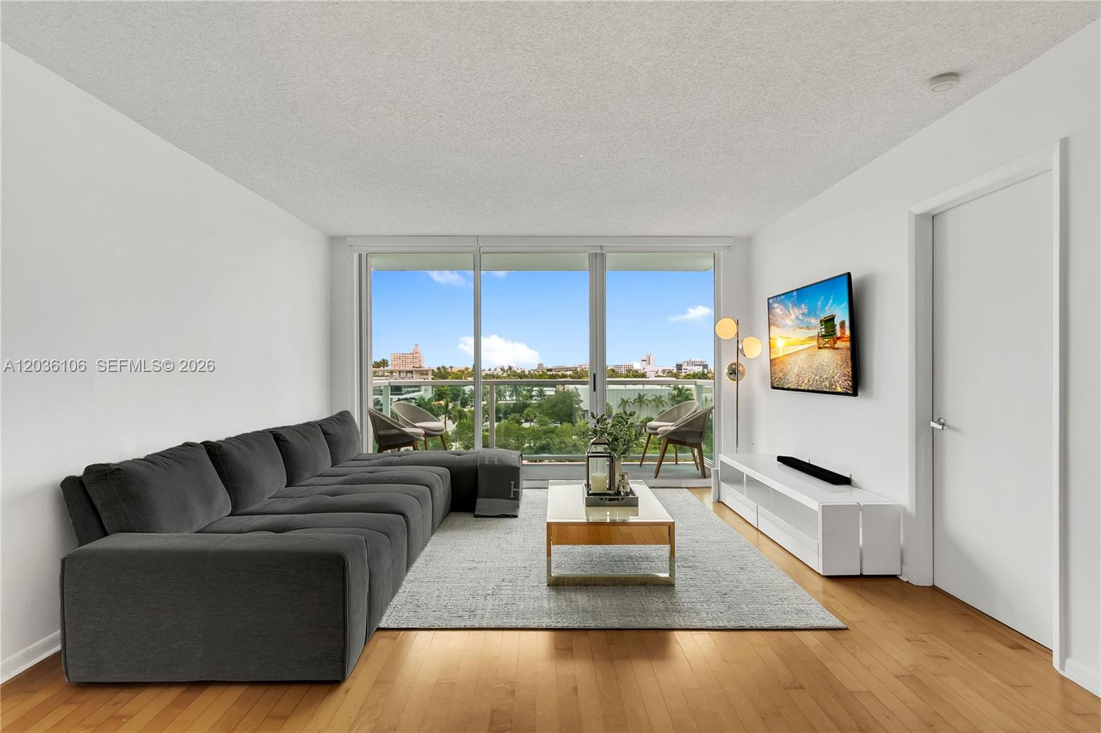 A living room features a gray sectional sofa, white media console, and floor-to-ceiling balcony windows — 650 West Ave # 704, Miami Beach FL 33139, MIAMI BEACH, FL