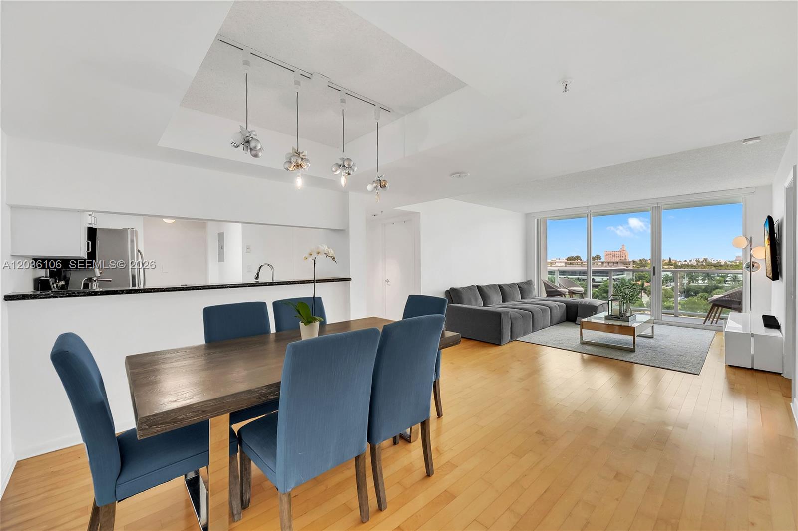 An open-concept living and dining area features blue chairs, hardwood floors, and a balcony view — 650 West Ave # 704, Miami Beach FL 33139, MIAMI BEACH, FL