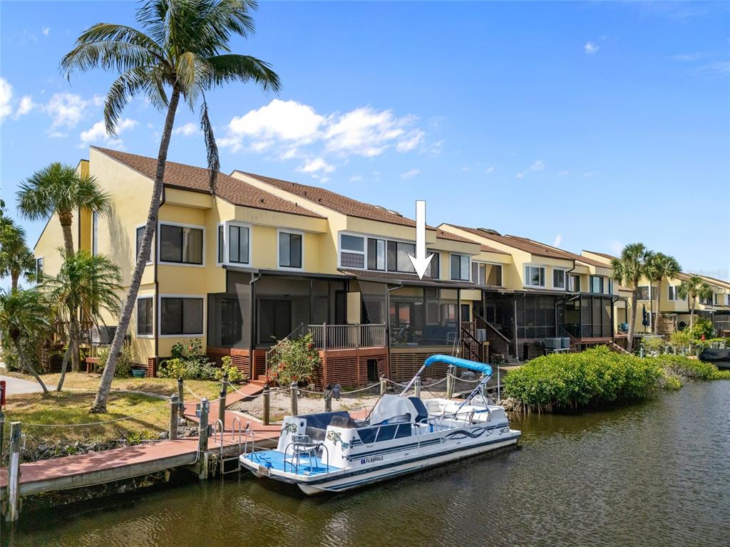 A yellow multi-story townhouse with a screened-in deck sits beside a canal with a pontoon boat — 25188 MARION AVENUE UNIT 1038, PUNTA GORDA, FL