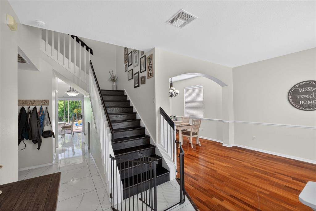 A staircase with dark wood steps and a safety gate sits between tiled and hardwood floors — 14903 YORKSHIRE RUN DRIVE, ORLANDO, FL