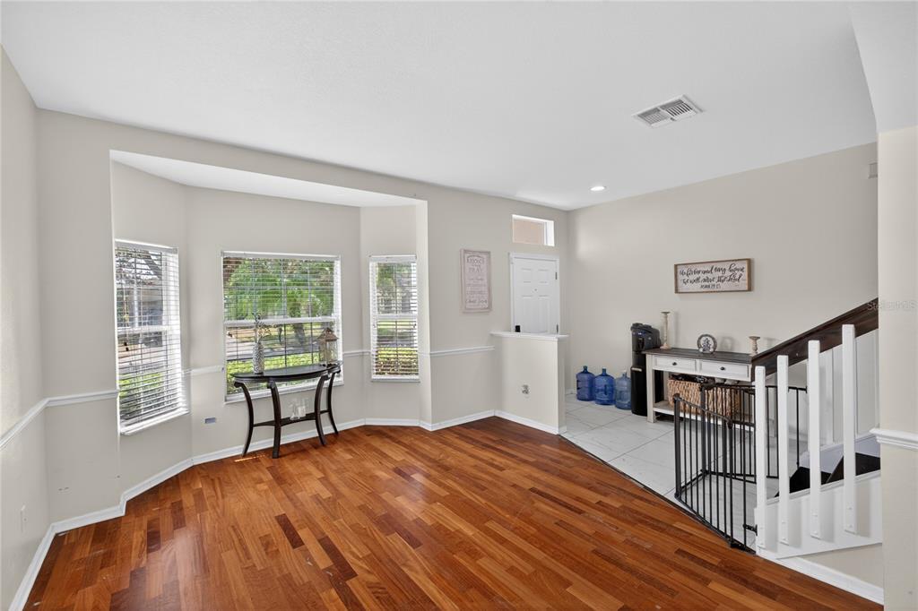 An empty room with hardwood floors, a bay window, and a staircase with white railings — 14903 YORKSHIRE RUN DRIVE, ORLANDO, FL