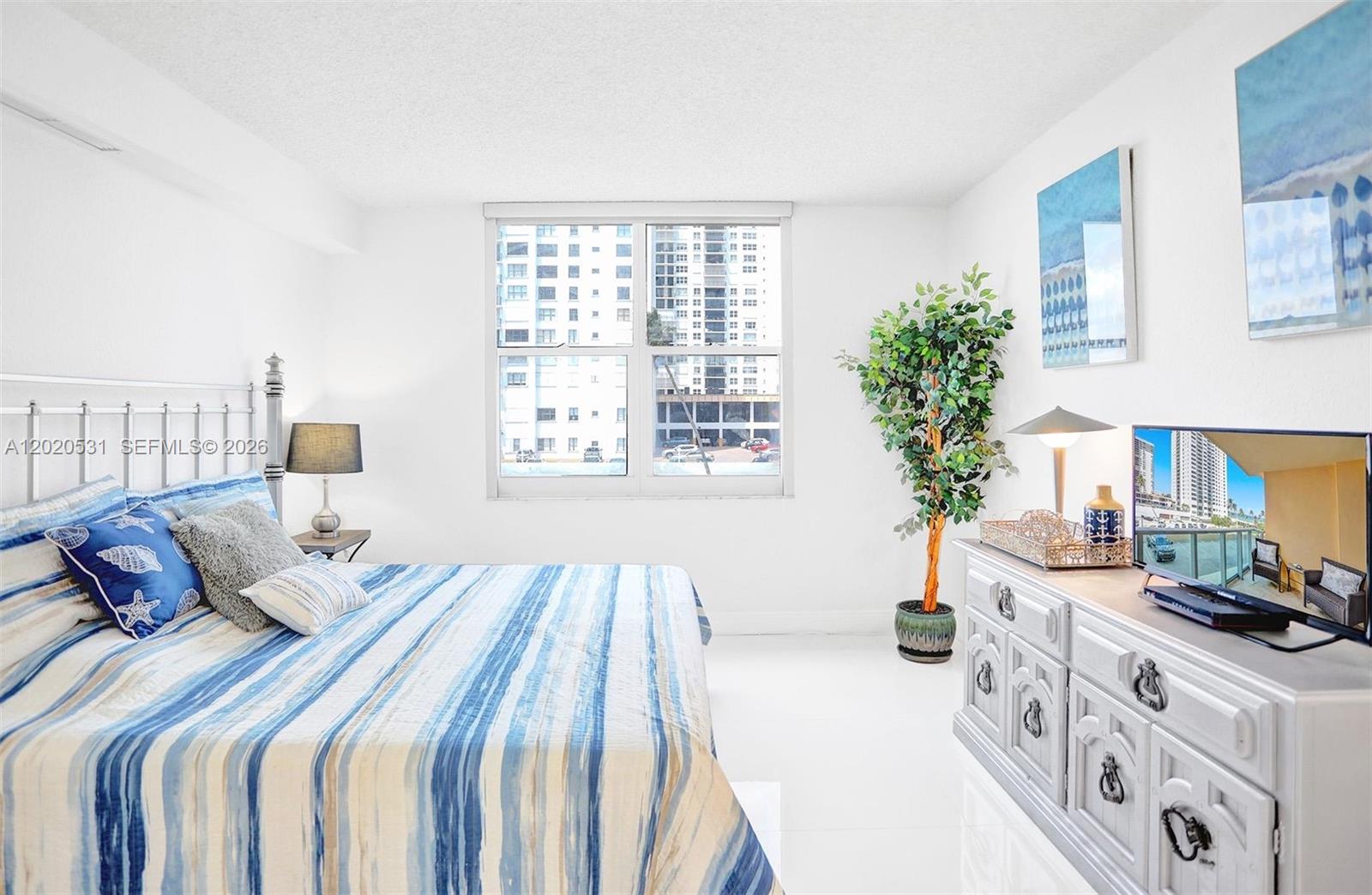 A bedroom features a bed with blue striped bedding, a white dresser, and a window — 2501 S Ocean Dr, Hollywood FL 33019, HOLLYWOOD, FL