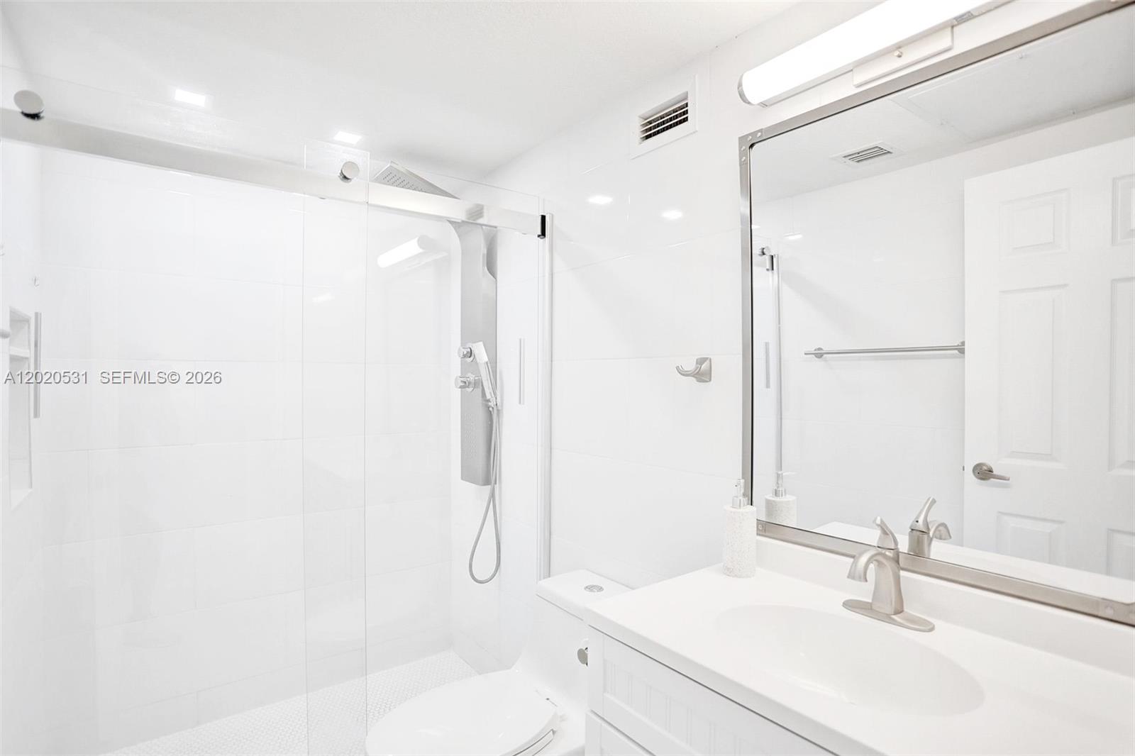 A bright, all-white bathroom features a glass-enclosed walk-in shower and a vanity with a mirror — 2501 S Ocean Dr, Hollywood FL 33019, HOLLYWOOD, FL