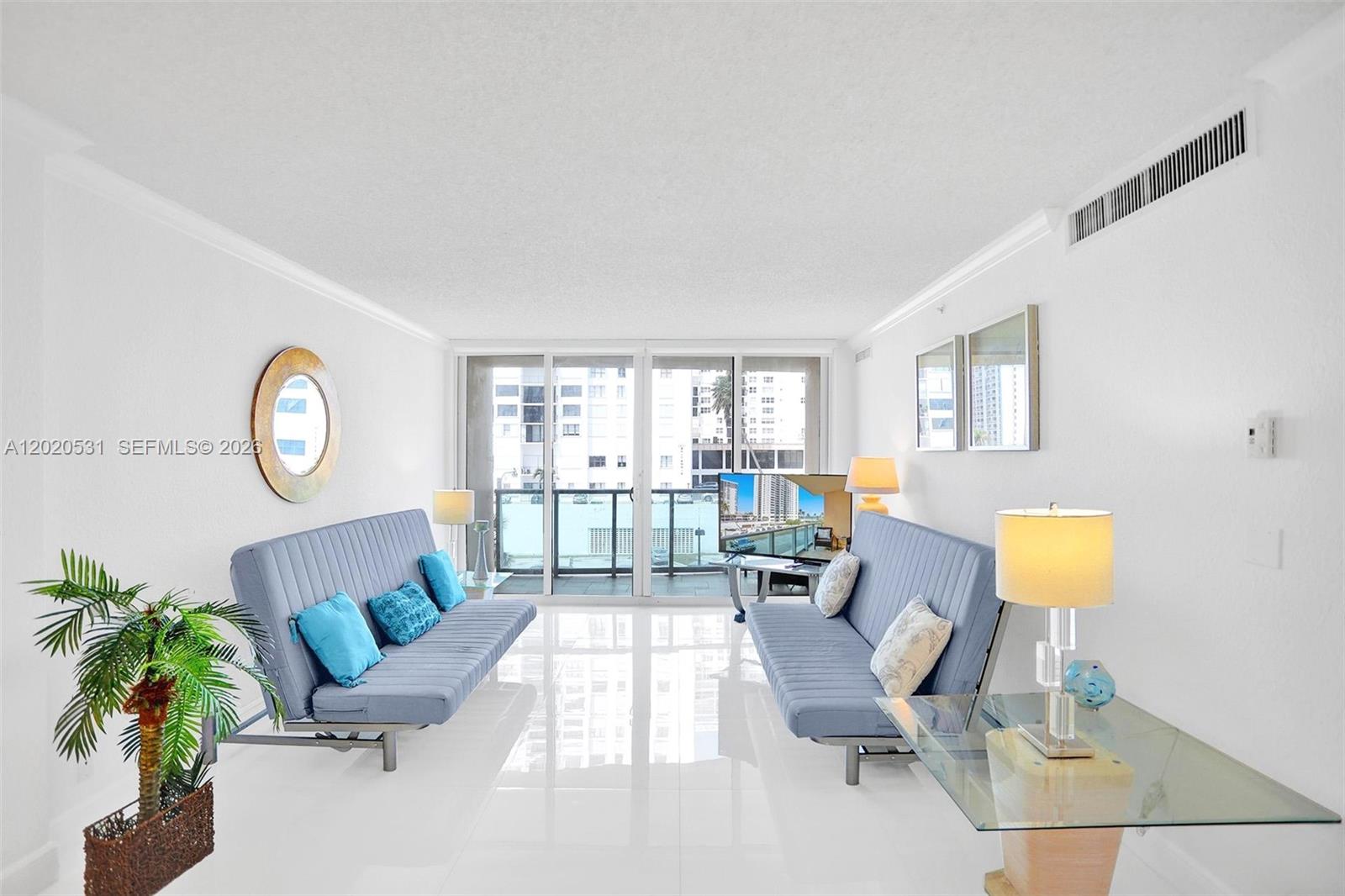 A bright living room features white tile floors, two blue sofas, and a balcony view — 2501 S Ocean Dr, Hollywood FL 33019, HOLLYWOOD, FL