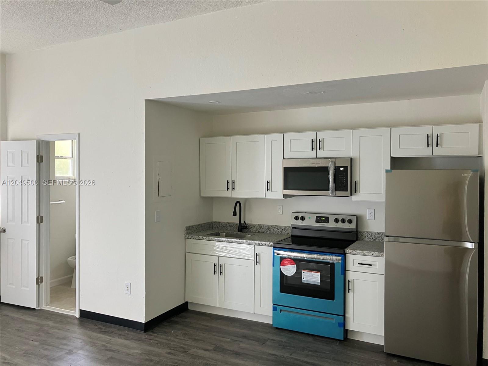 A kitchen features white cabinets, stainless steel appliances, and granite countertops next to a bathroom — 467 NW 8th St # 4, Miami FL 33136, MIAMI, FL