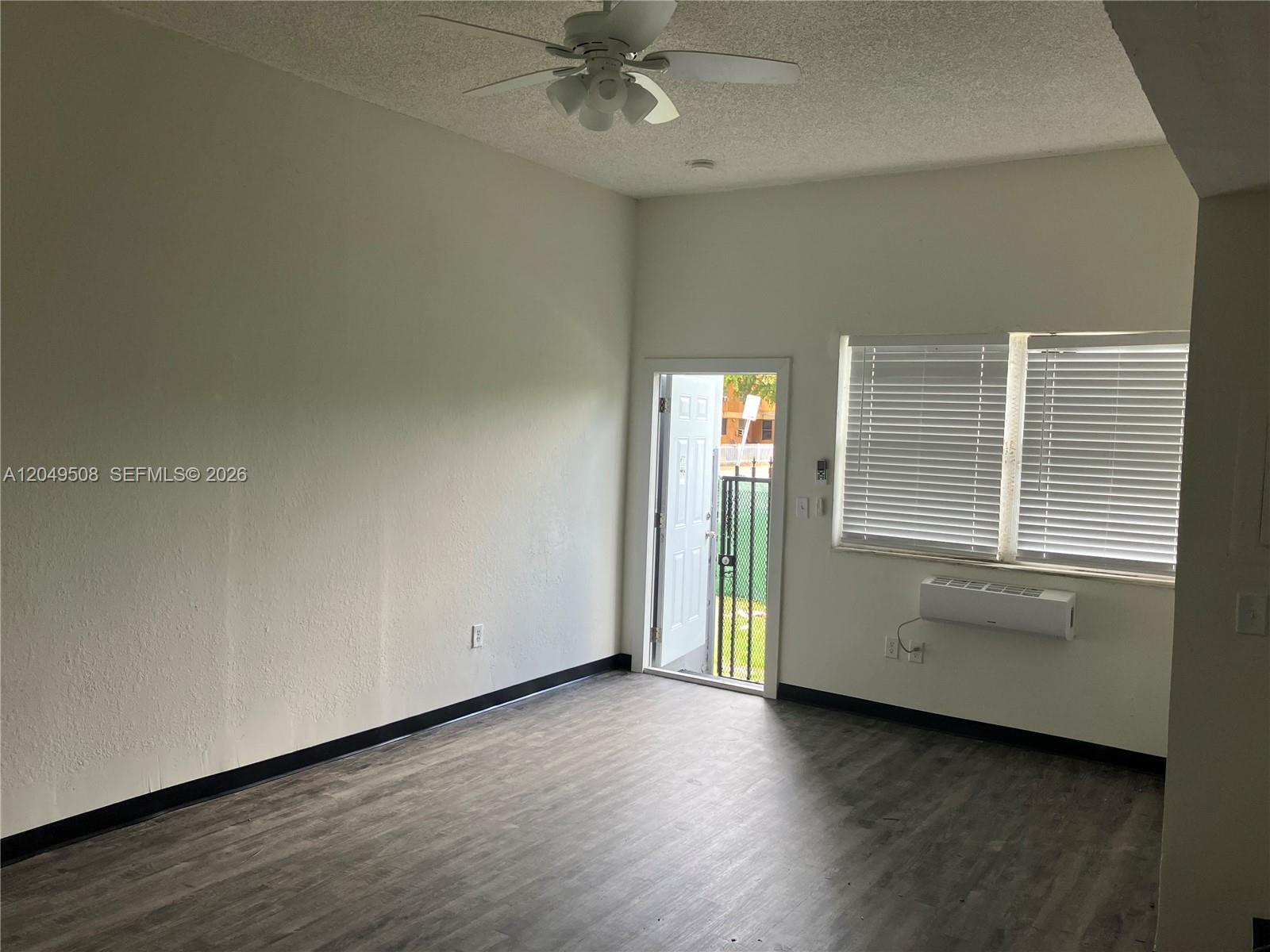 An empty room features wood-look flooring, a ceiling fan, a window unit, and an exterior door — 467 NW 8th St # 4, Miami FL 33136, MIAMI, FL