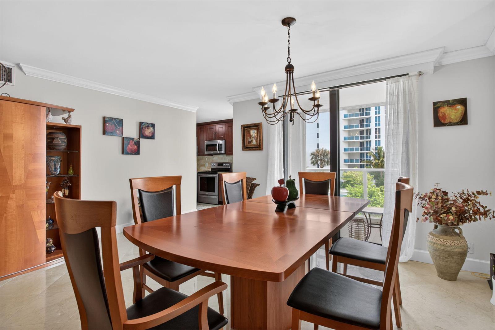 A dining room features a wooden table, six chairs, a chandelier, and a balcony view — 1000 S Ocean Boulevard # 5j, Pompano Beach FL 33062, POMPANO BEACH, FL