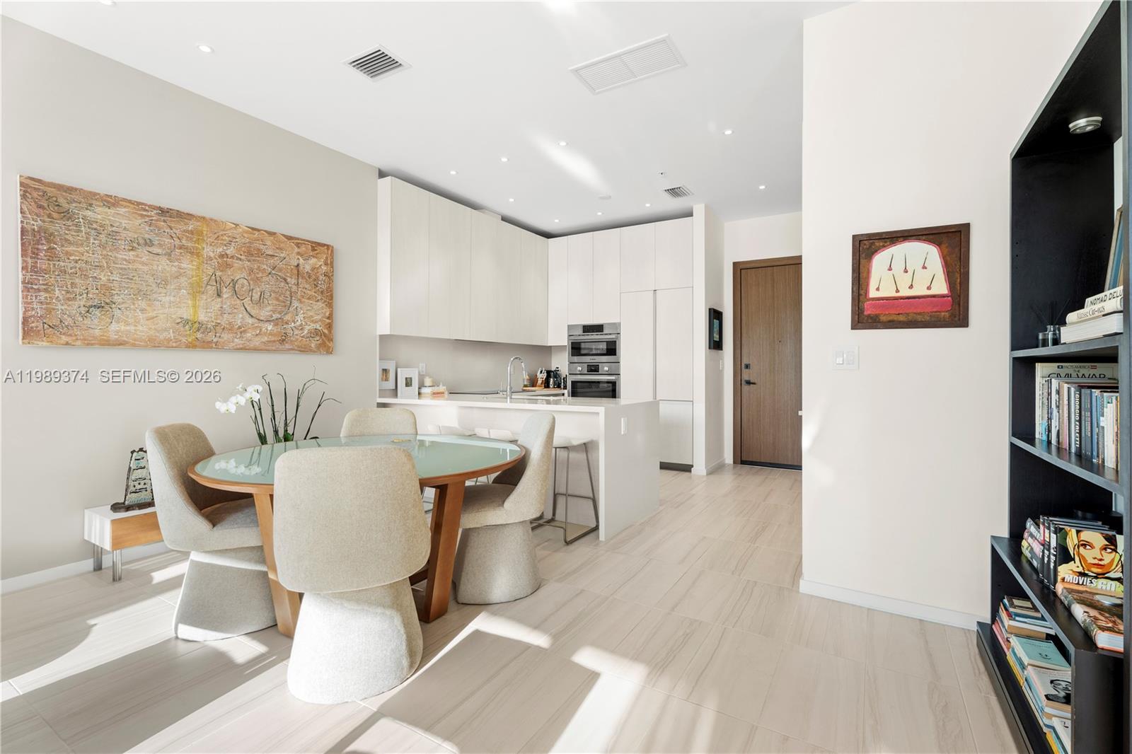 A modern kitchen and dining area with a glass-topped table, white cabinetry, and tile flooring — 3156 SW 27th Ave # 202, Miami FL 33133, MIAMI, FL