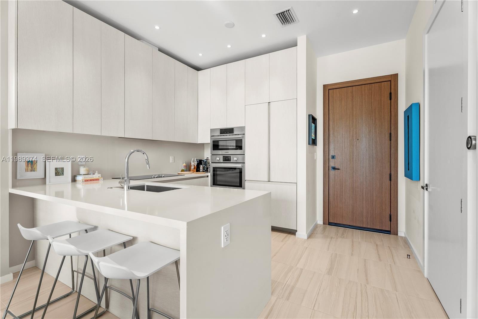 A modern kitchen features white cabinetry, a quartz island with bar seating, and stainless appliances — 3156 SW 27th Ave # 202, Miami FL 33133, MIAMI, FL